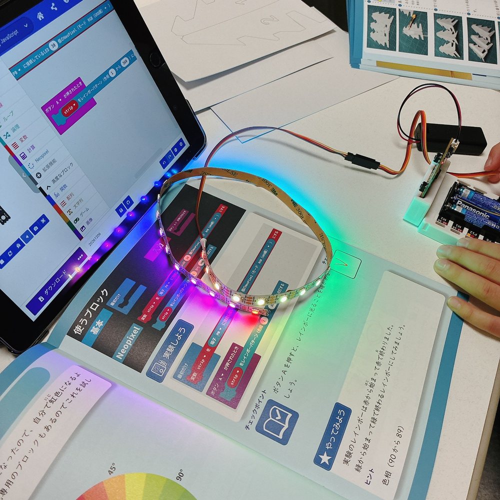 テキストとタブレットのMakeCodeを見ながら、micro:bitにつないだ外付けのフルカラーLEDテープを光らせている様子